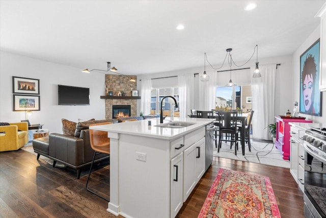 kitchen featuring dark wood finished floors, stainless steel appliances, open floor plan, a sink, and a stone fireplace