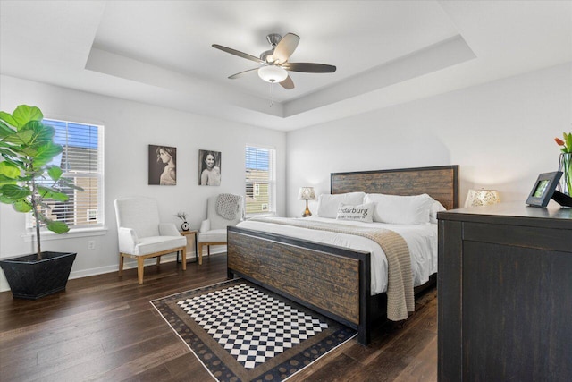 bedroom with ceiling fan, baseboards, a raised ceiling, and dark wood-style flooring