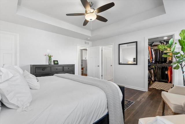 bedroom with visible vents, baseboards, a raised ceiling, wood finished floors, and a walk in closet