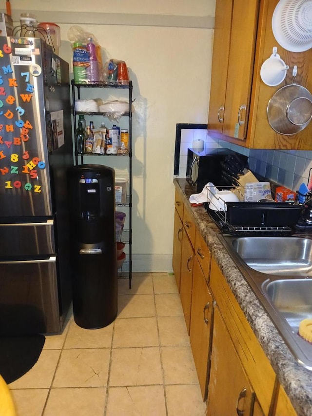 kitchen featuring light tile patterned floors, decorative backsplash, brown cabinetry, freestanding refrigerator, and a sink