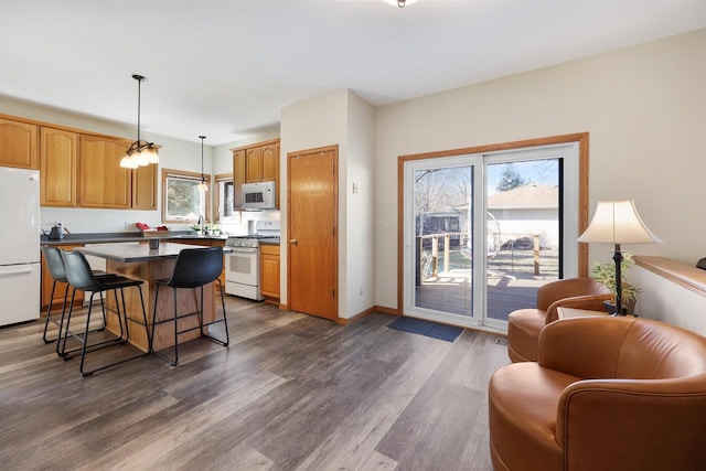 kitchen with a center island, pendant lighting, a breakfast bar area, dark wood-style floors, and white appliances