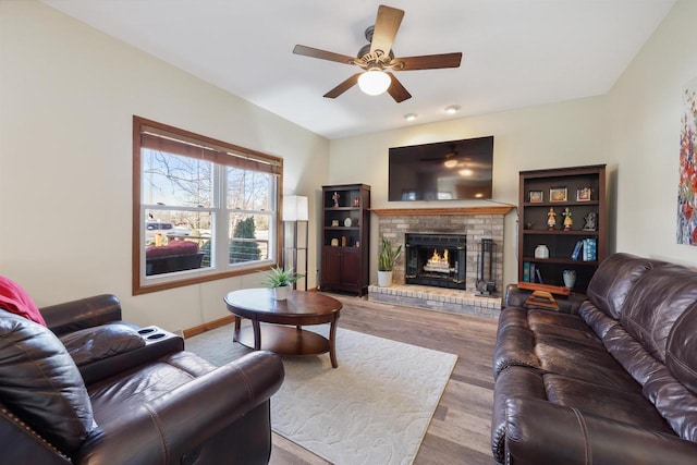 living room with a ceiling fan, a brick fireplace, wood finished floors, and baseboards