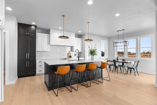 kitchen with a sink, light countertops, hanging light fixtures, light wood-type flooring, and a center island with sink