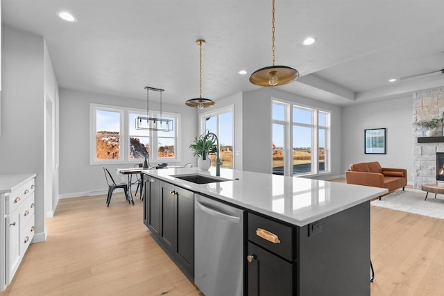 kitchen with light countertops, stainless steel dishwasher, a kitchen island with sink, and dark cabinetry