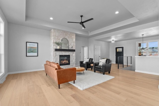 living room with a ceiling fan, a tray ceiling, a fireplace, and light wood finished floors