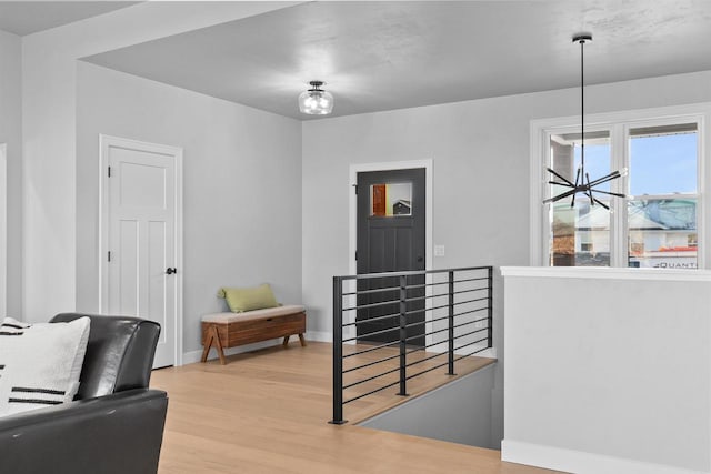 living area with a chandelier, light wood-type flooring, an upstairs landing, and baseboards