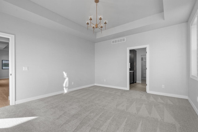 unfurnished room with light carpet, a tray ceiling, visible vents, and an inviting chandelier