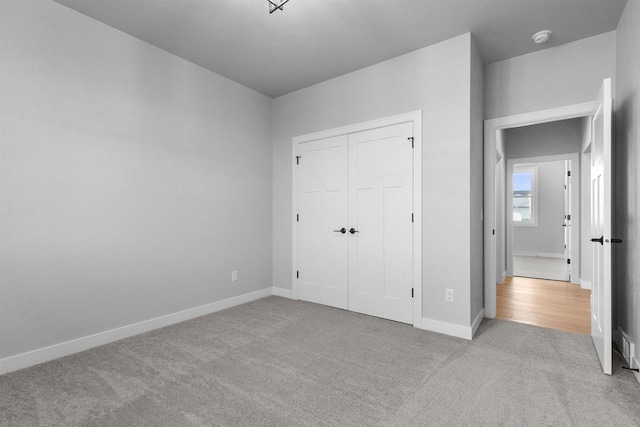 unfurnished bedroom with light carpet, a closet, and baseboards