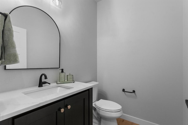 half bath featuring baseboards, vanity, toilet, and wood finished floors