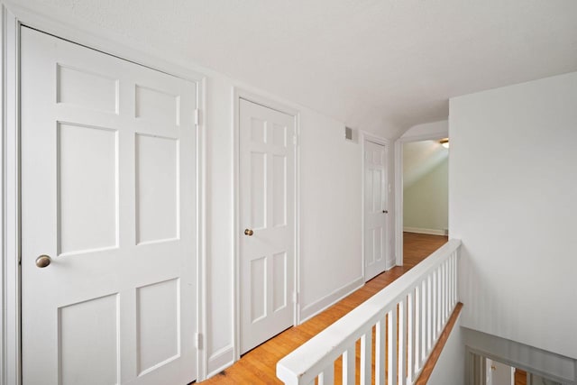 corridor featuring lofted ceiling, visible vents, light wood-style floors, an upstairs landing, and baseboards