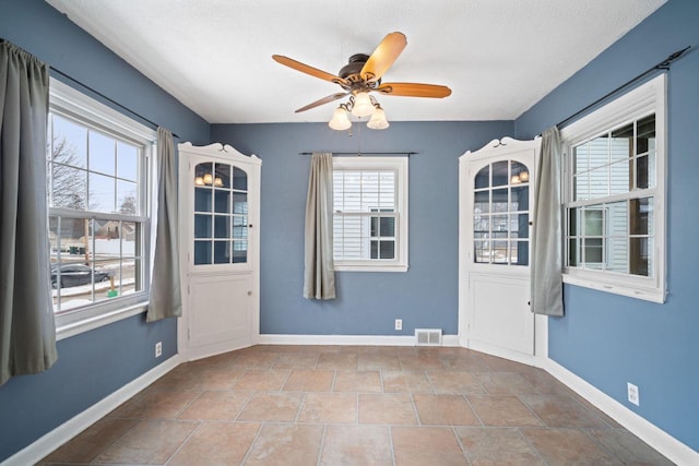 spare room featuring a textured ceiling, a ceiling fan, visible vents, and baseboards