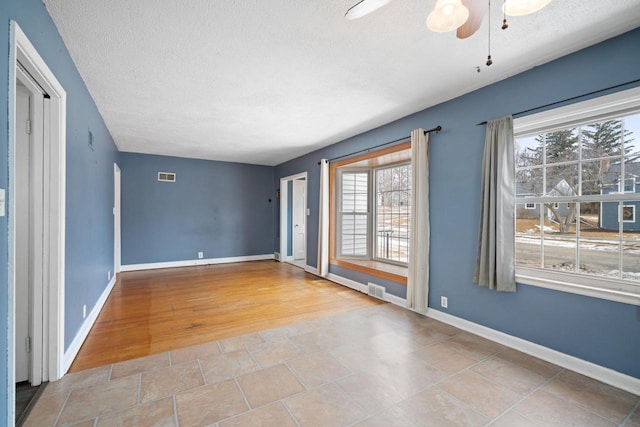 spare room featuring a ceiling fan, baseboards, visible vents, and a textured ceiling