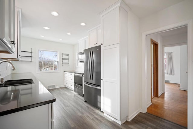 kitchen featuring stainless steel appliances, visible vents, white cabinetry, a sink, and wood finished floors