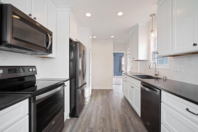 kitchen featuring dark countertops, appliances with stainless steel finishes, hanging light fixtures, white cabinetry, and a sink