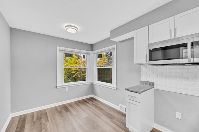 unfurnished dining area with light wood finished floors, visible vents, and baseboards