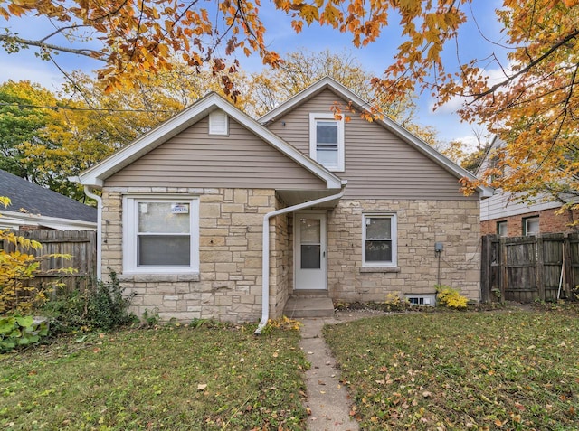 bungalow featuring a front yard, stone siding, and fence