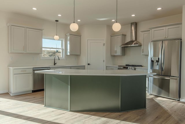 kitchen featuring wall chimney exhaust hood, a kitchen island, stainless steel appliances, light countertops, and a sink