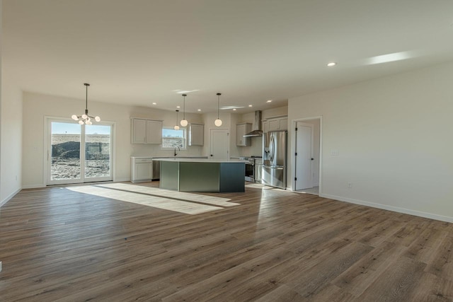 kitchen featuring open floor plan, wall chimney range hood, a kitchen island, and appliances with stainless steel finishes