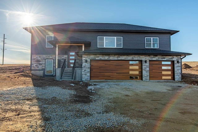 view of front of home with stone siding, an attached garage, and dirt driveway