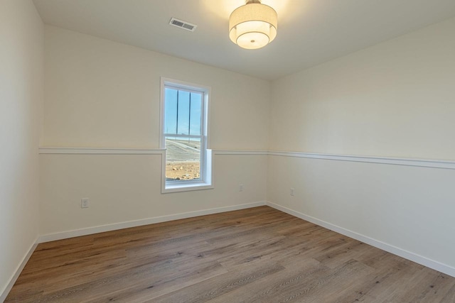 empty room featuring wood finished floors, visible vents, and baseboards