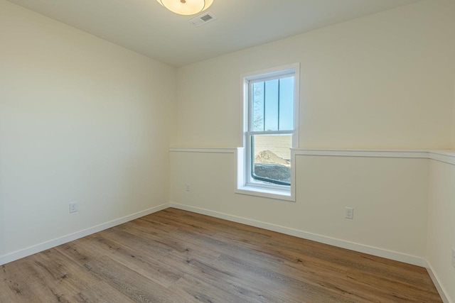 spare room with wood finished floors, visible vents, and baseboards