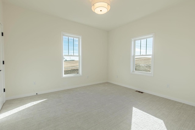 spare room featuring visible vents, a healthy amount of sunlight, light carpet, and baseboards