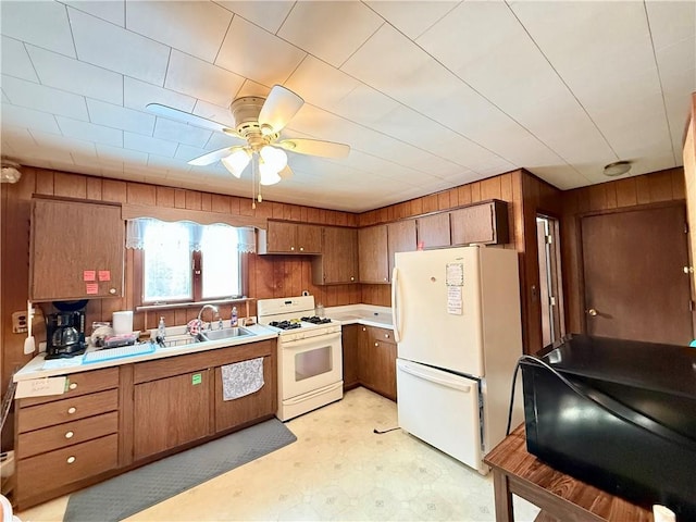 kitchen with white appliances, wooden walls, light countertops, light floors, and a sink