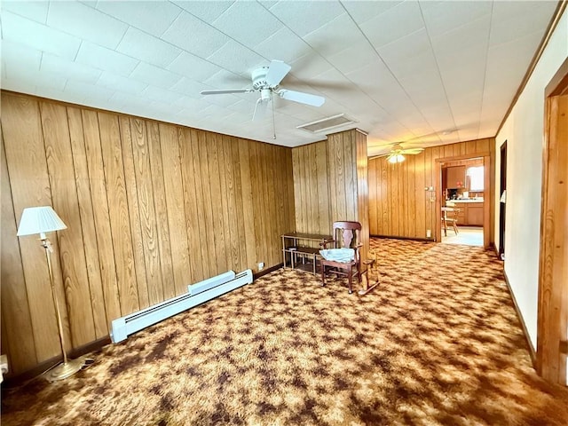 unfurnished room featuring a baseboard radiator, a ceiling fan, carpet flooring, wooden walls, and baseboards