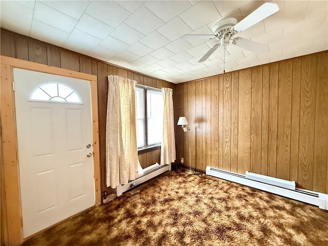 entryway with a ceiling fan, a baseboard radiator, wood walls, and dark colored carpet