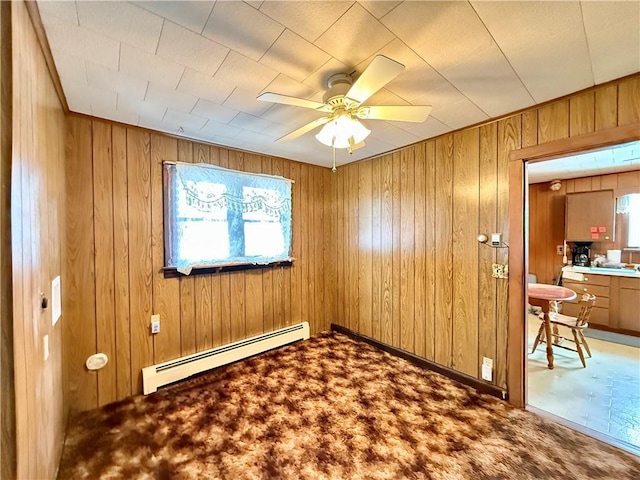 spare room featuring carpet floors, wooden walls, baseboard heating, and a ceiling fan