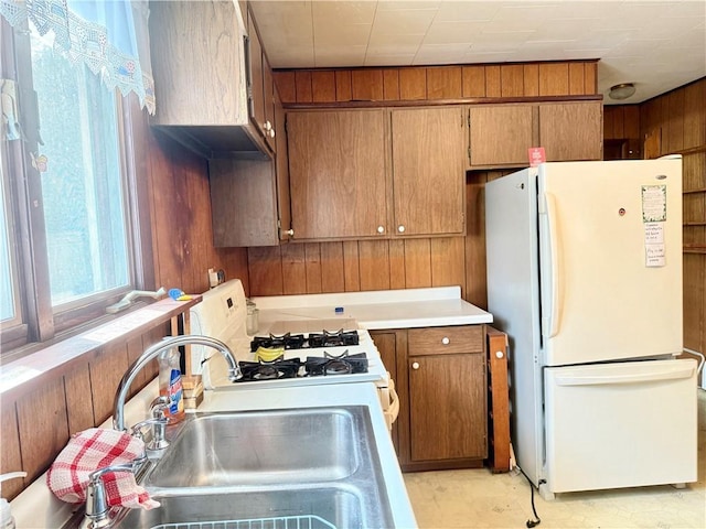 kitchen featuring light countertops, white appliances, a sink, and brown cabinets