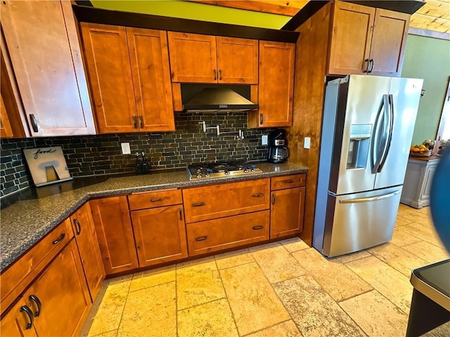 kitchen featuring stone tile floors, decorative backsplash, appliances with stainless steel finishes, dark stone countertops, and wall chimney exhaust hood