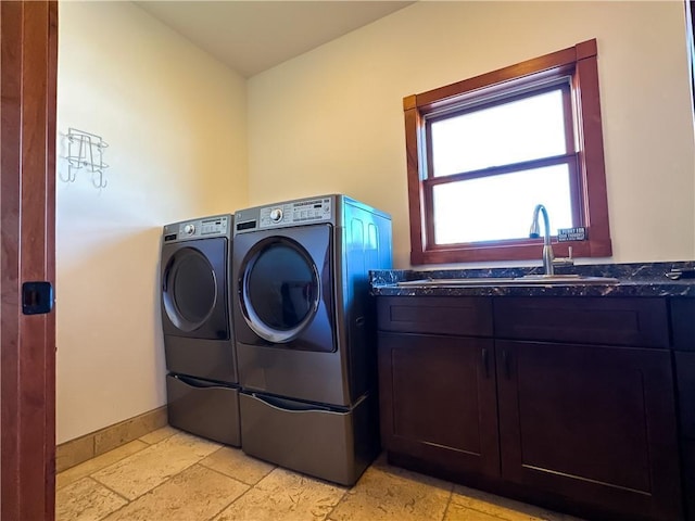 laundry room featuring washing machine and dryer, stone tile flooring, cabinet space, and a sink