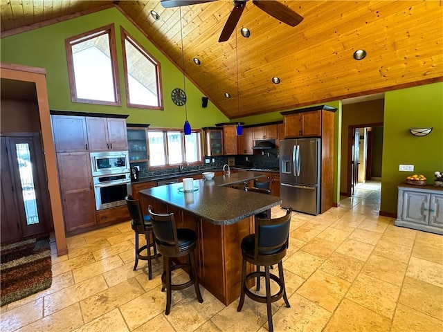 kitchen featuring wooden ceiling, under cabinet range hood, appliances with stainless steel finishes, an island with sink, and dark countertops