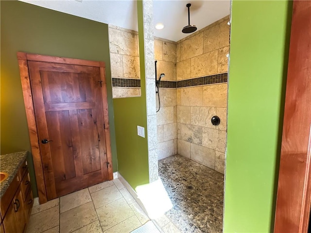 full bathroom with vanity, a tile shower, and stone tile flooring