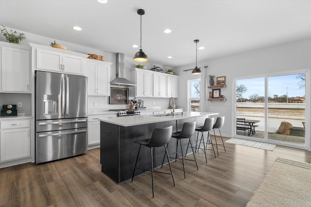kitchen featuring stainless steel refrigerator with ice dispenser, wall chimney exhaust hood, a sink, light countertops, and dark wood-style flooring