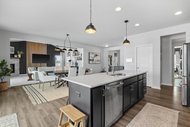 kitchen with appliances with stainless steel finishes, a sink, light countertops, a fireplace, and hanging light fixtures