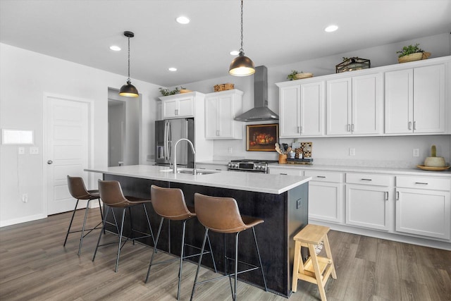 kitchen with wall chimney range hood, stainless steel appliances, wood finished floors, white cabinetry, and recessed lighting