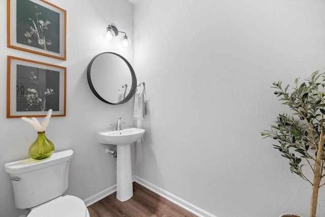 half bath featuring wood finished floors, toilet, and baseboards
