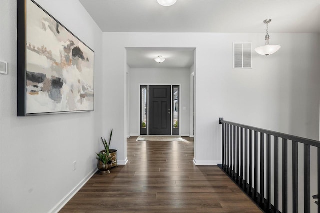 hall featuring dark wood-style flooring, baseboards, and an upstairs landing