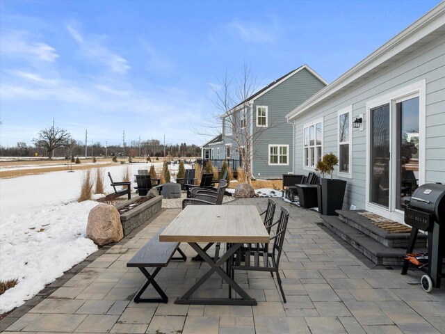 snow covered patio with outdoor dining space and grilling area