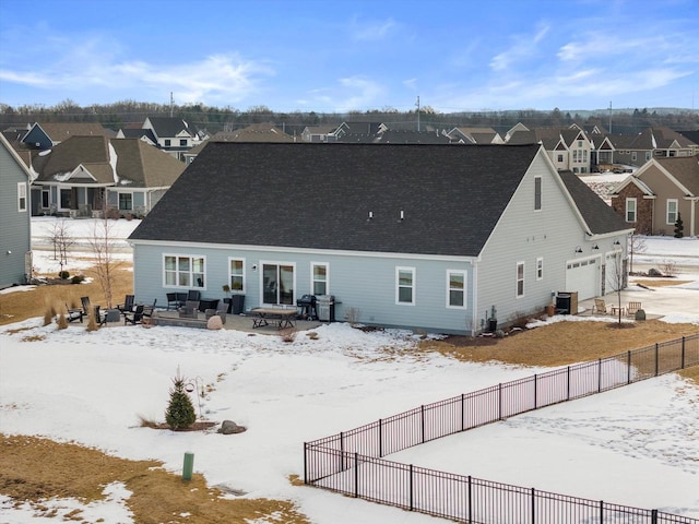 snow covered back of property with a garage, fence, central AC unit, roof with shingles, and a residential view