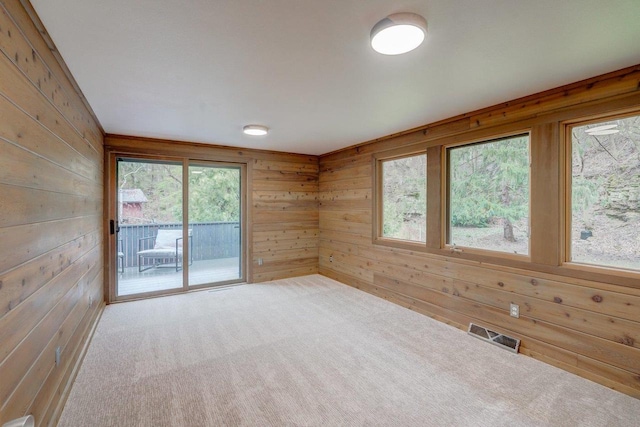 unfurnished room featuring carpet floors, wood walls, a healthy amount of sunlight, and visible vents