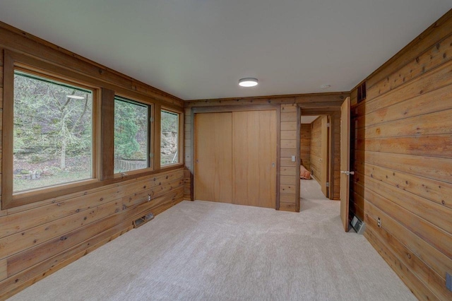 unfurnished bedroom with wooden walls, carpet, visible vents, and multiple windows