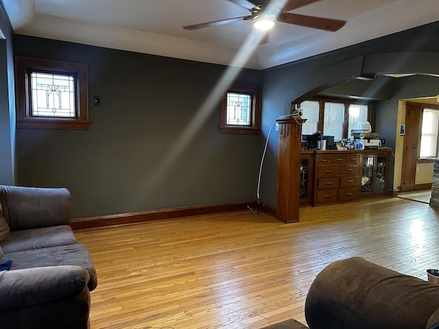 living area with baseboards, arched walkways, a ceiling fan, and light wood-style floors