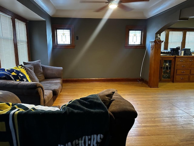 living room featuring light wood-style flooring, baseboards, arched walkways, and a ceiling fan