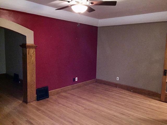 unfurnished room with arched walkways, wood finished floors, visible vents, baseboards, and a ceiling fan