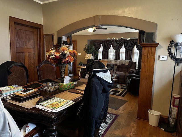 dining area with arched walkways, ceiling fan, and wood finished floors