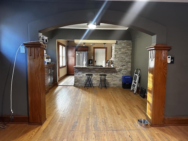 bar featuring arched walkways, light wood-style flooring, freestanding refrigerator, and baseboards