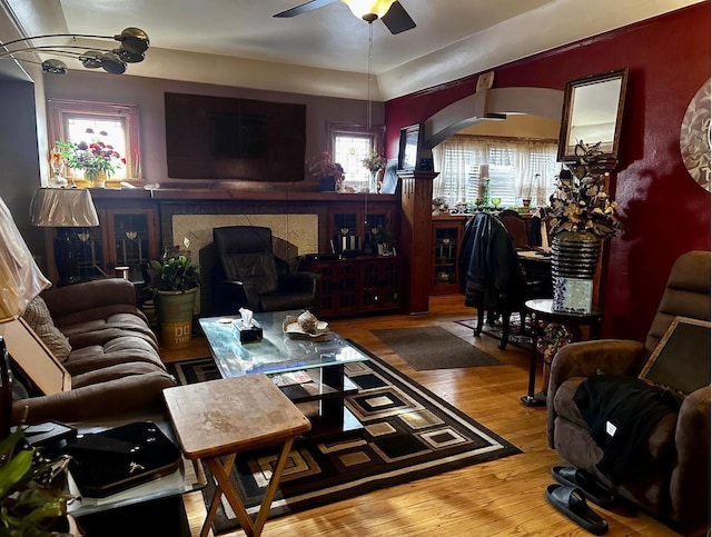 living room featuring light wood-style floors, ceiling fan, a fireplace, and arched walkways